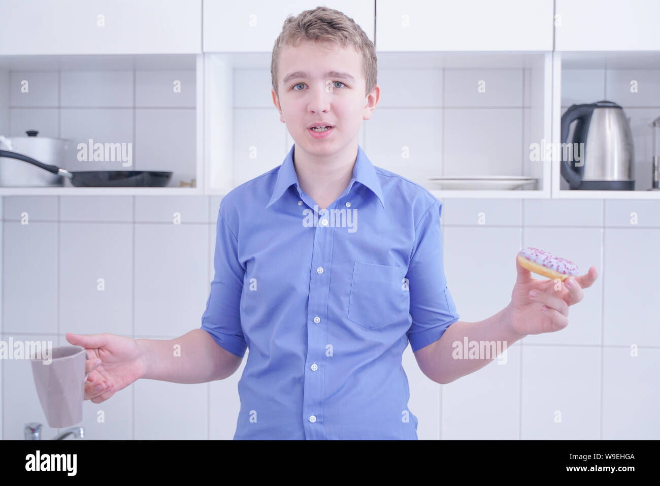 Little happy cute boy is eating donut on white kitchen background alone ...