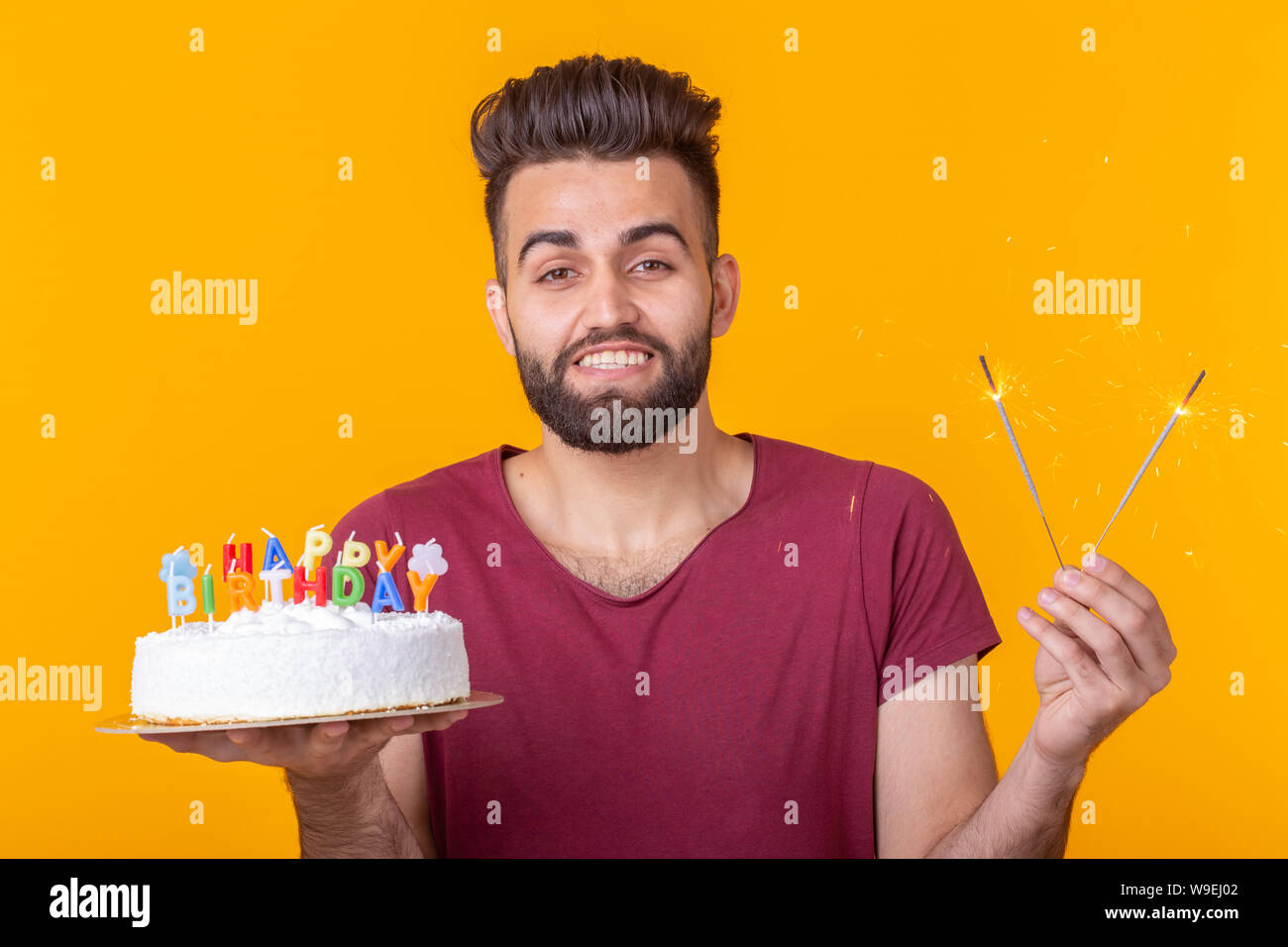 Positive Young Man Holding A Happy Birthday Cake And Two Burning Bengal Lights Posing On A Yellow Background Stock Photo Alamy