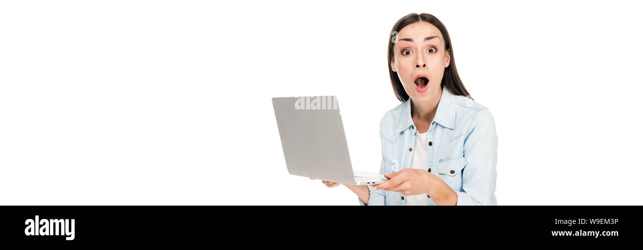 shocked girl in denim jacket holding laptop isolated on white, panoramic shot Stock Photo