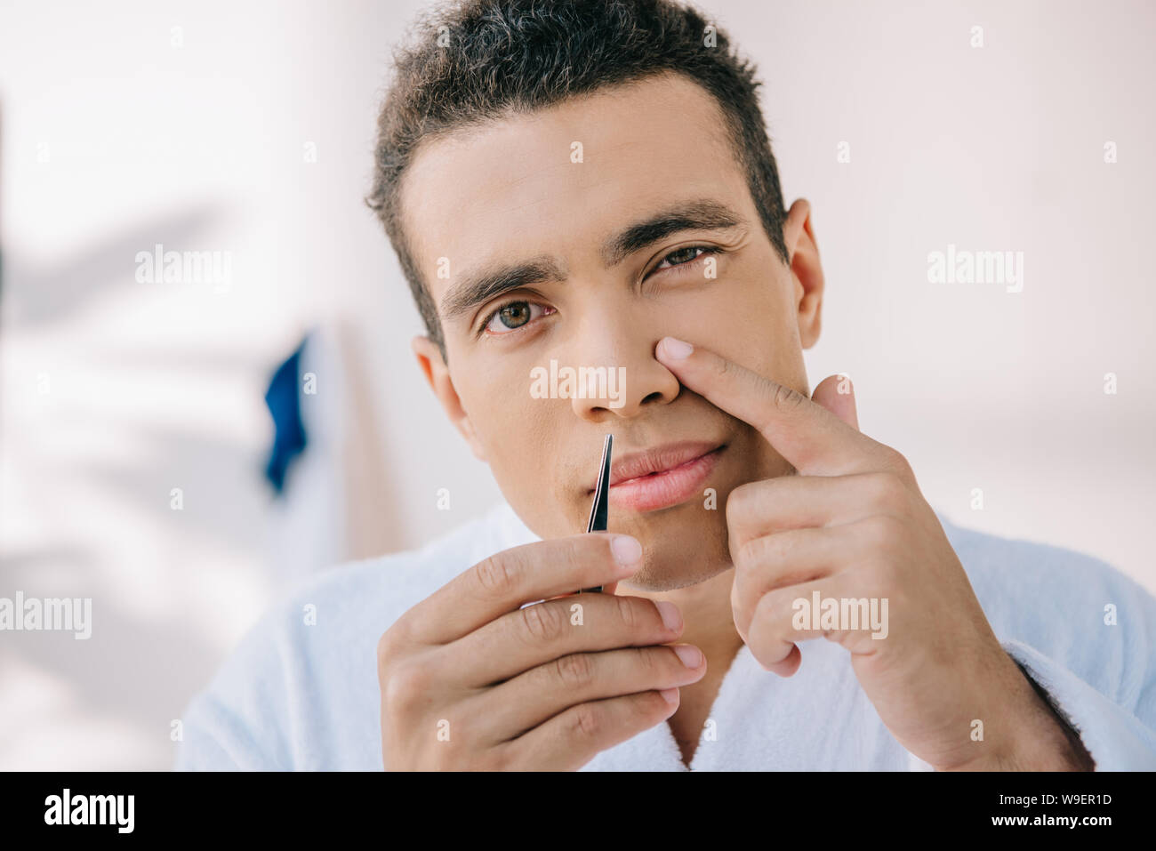 Handsome Young Man Plucking Nose With Tweezer And Looking At