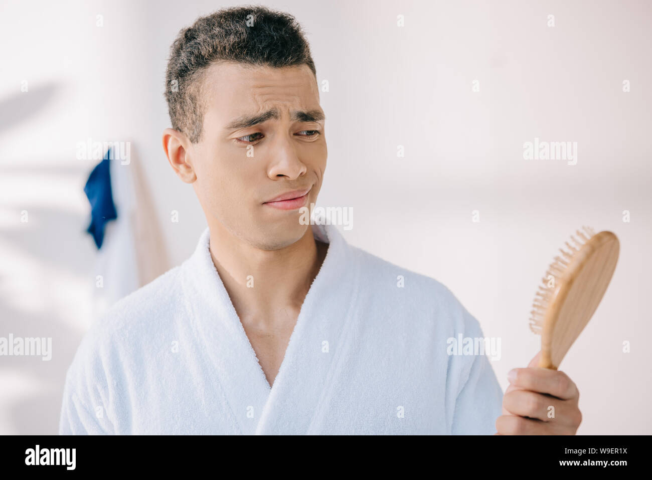 disappointed young man in bathrobe holding hairbrush Stock Photo