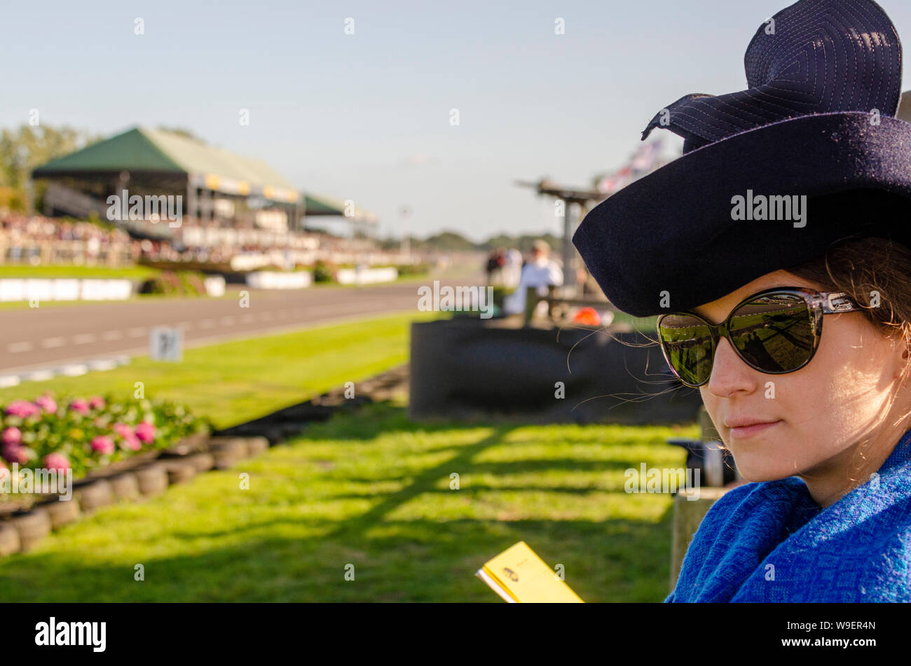 Glamorous female in period attire watching the race circuit motor racing at the Goodwood Revival on a sunny day. Girl in vintage dress Stock Photo