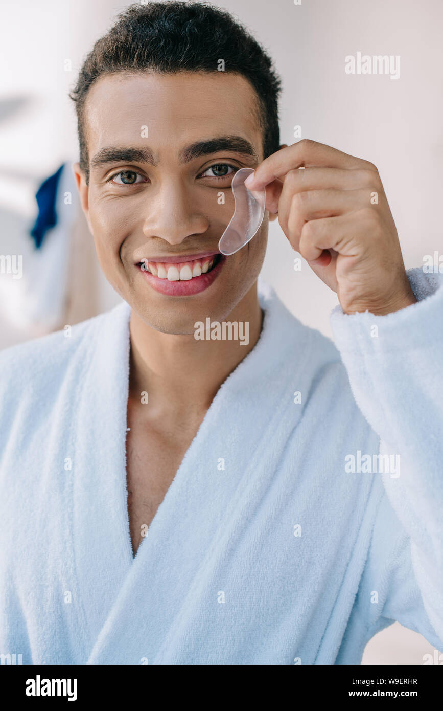 handsome young man in bathrobe showing patch and smiling while looking at camera Stock Photo