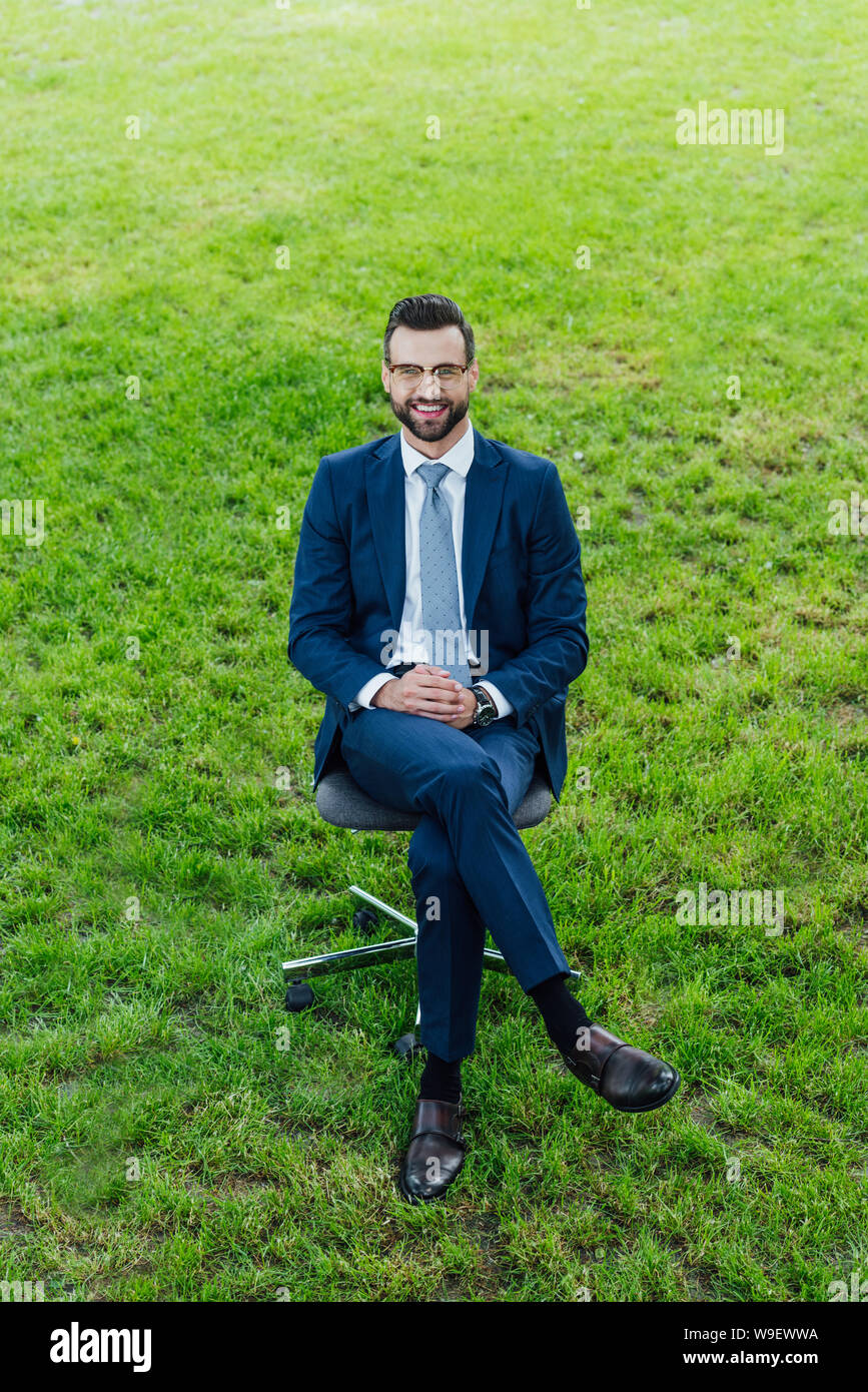 high angle view of happy young businessman sitting in office chair in park and loooking at camera Stock Photo
