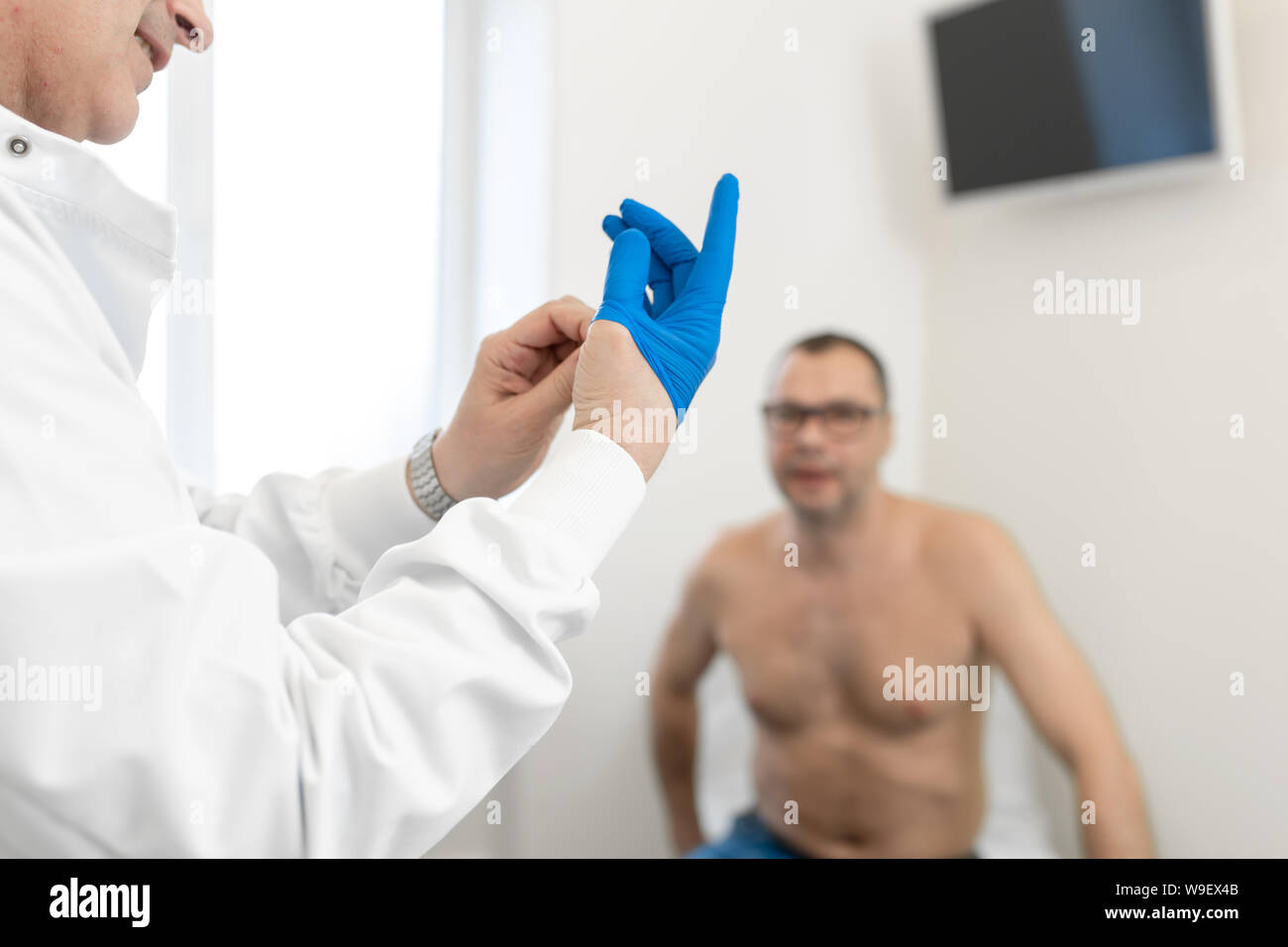 Doctor urologist puts a medical glove on the arm to examine the patient's prostate, prostate massage, lymphatic drainage. Stock Photo
