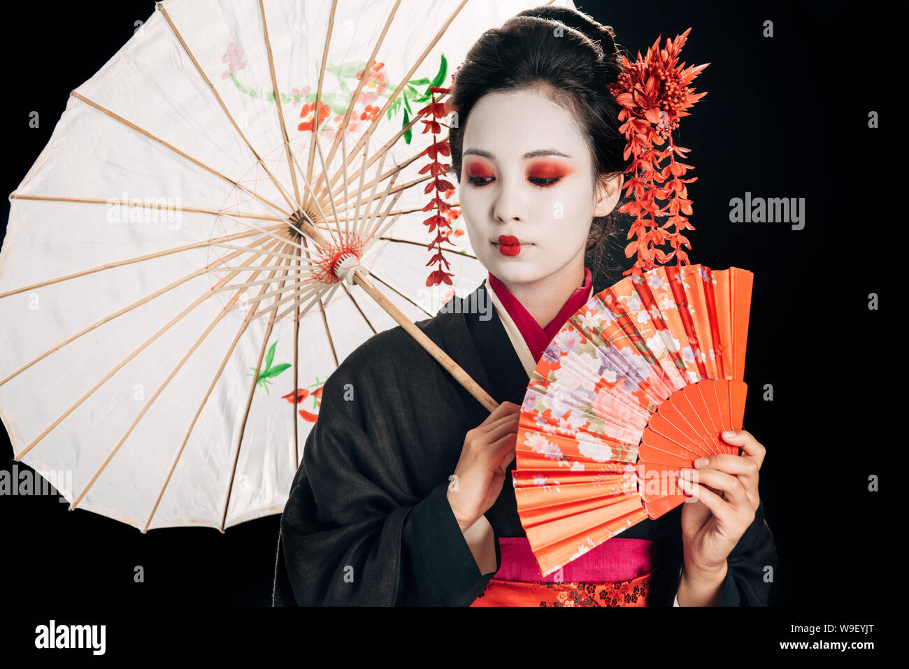beautiful geisha in black kimono with red flowers in hair holding traditional  asian umbrella and hand fan isolated on black Stock Photo - Alamy, image size:1300x957