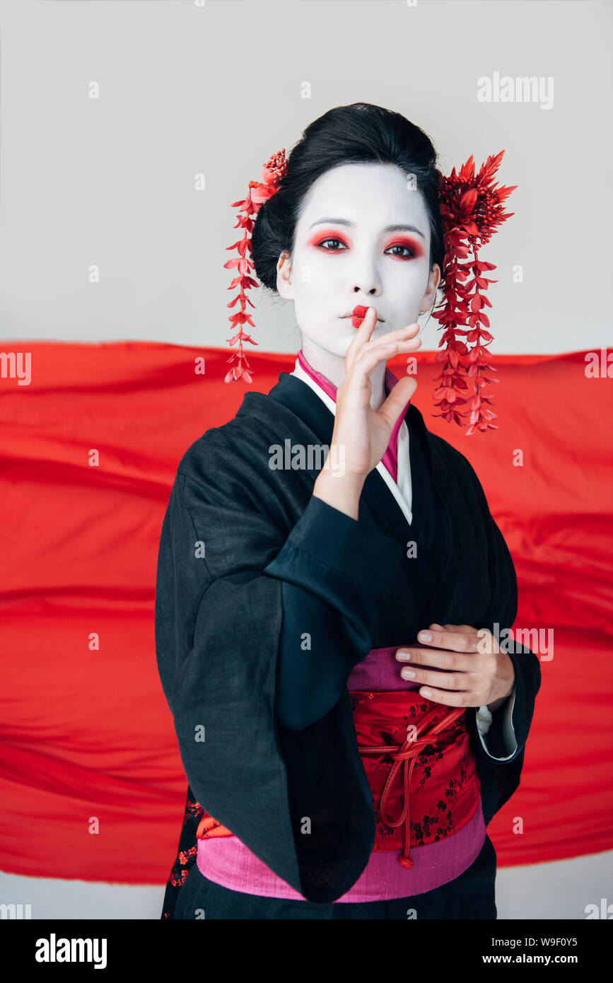 beautiful geisha in black kimono with red cloth on background showing shh sign isolated on white Stock Photo