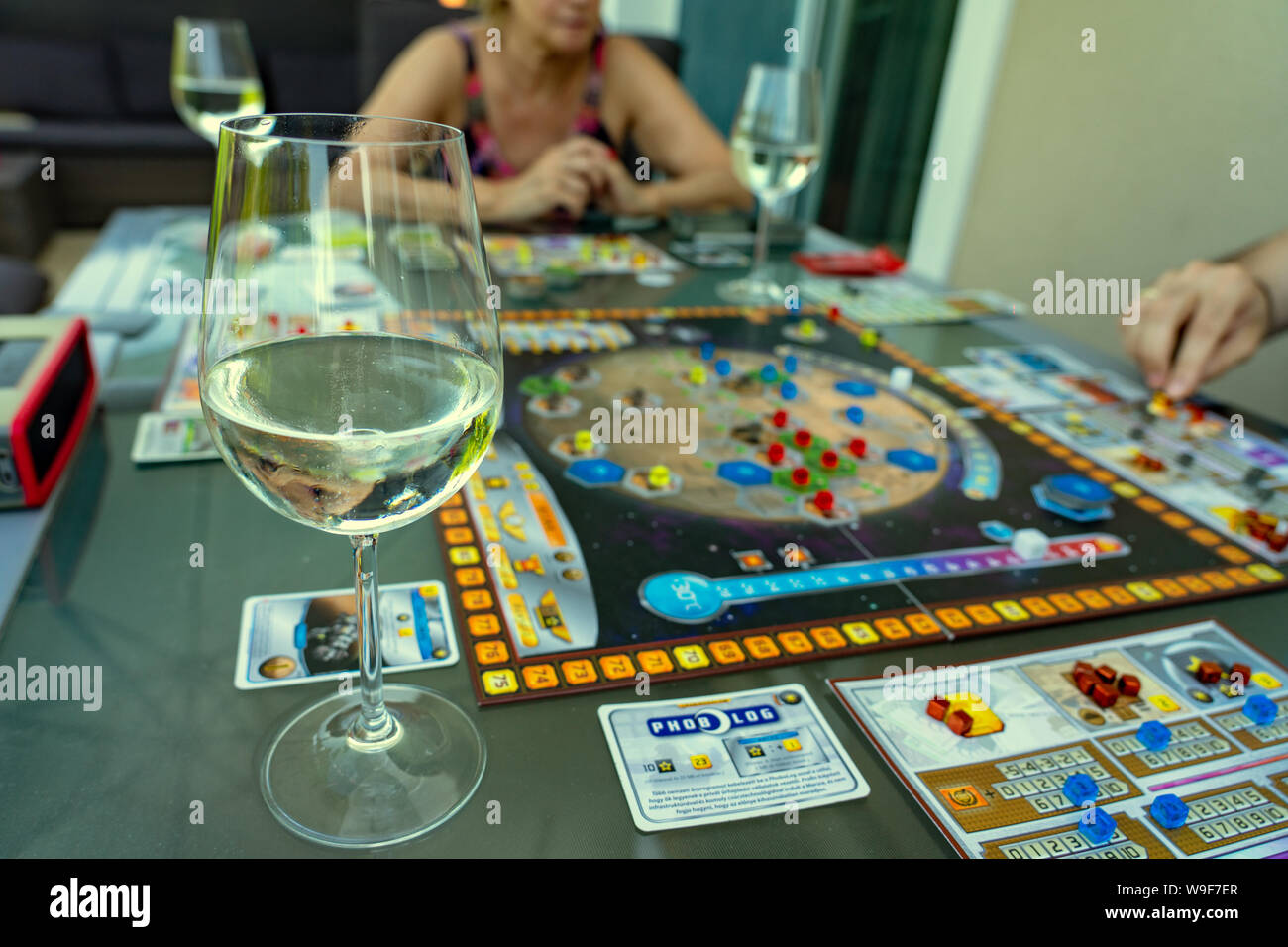 Balogunyom / Hungary - 08.12.2019: Glass of White wine with home entertainment Players playing board game Terraforming Mars strategy game Stock Photo