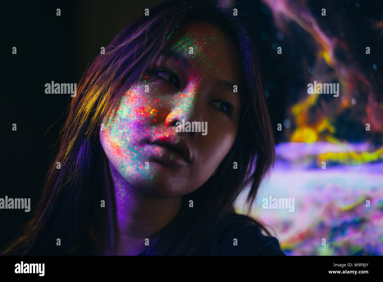 Beautiful young woman dancing and making party with fluorescent painting on her face. Neon facial portraits Stock Photo