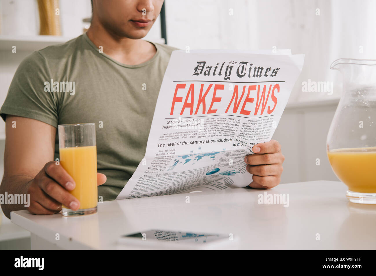 cropped view of young man reading fake news newspaper while sitting at ...