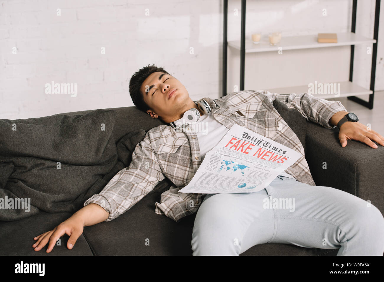 tired asian man sleeping on sofa at home with fake news newspaper Stock Photo