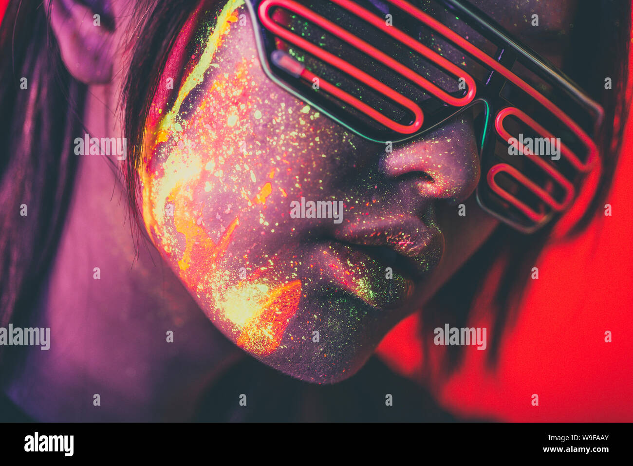 Beautiful young woman dancing and making party with fluorescent painting on her face. Neon facial portraits Stock Photo