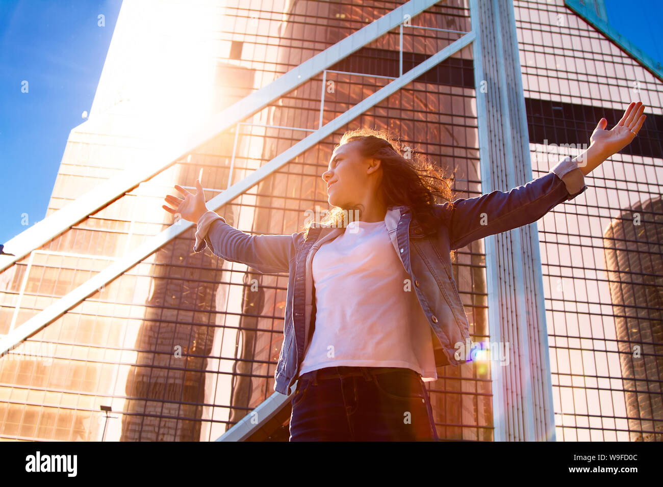 Young girl with her hands wide open with the city in the background. Concept of freedom. The love and emotions, a woman's happiness. Sunset over the c Stock Photo