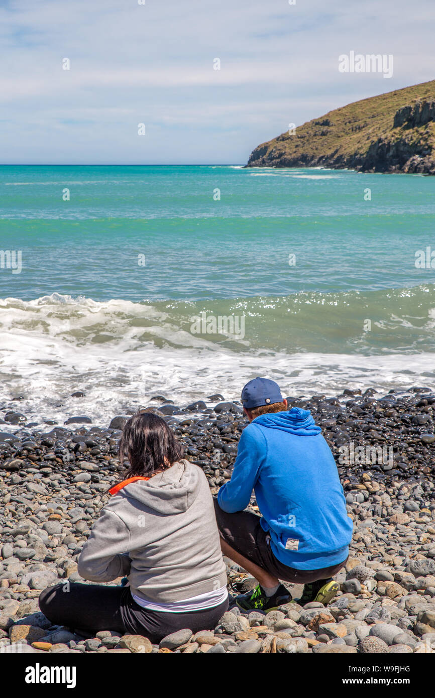 A couple enjoy the picturesque landscape at a bay in the Banks Peninsula area, summertime, Canterbury, New Zealand Stock Photo