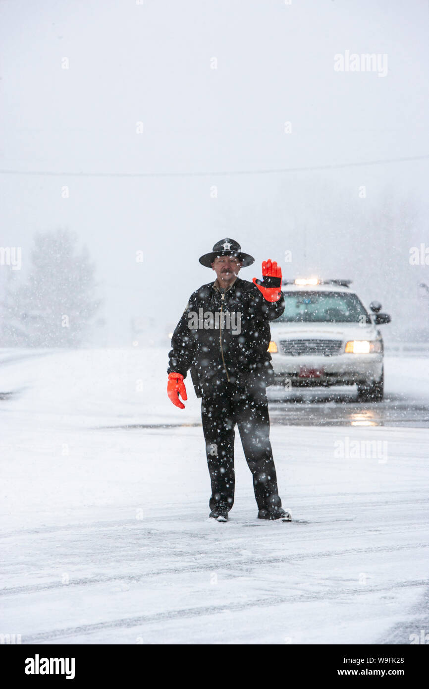 A winter blizzard stops traffic on the highway in southern Vermont as a patrolman directs oncoming cars Stock Photo