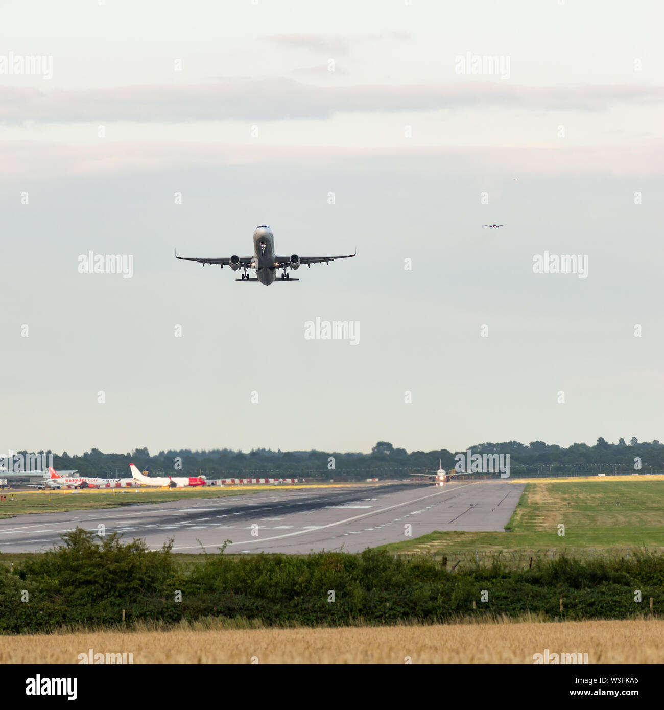An airplane takes off as others come into land in an aircraft landing queue behind, with other planes waiting next to the runway to takeoff. Stock Photo