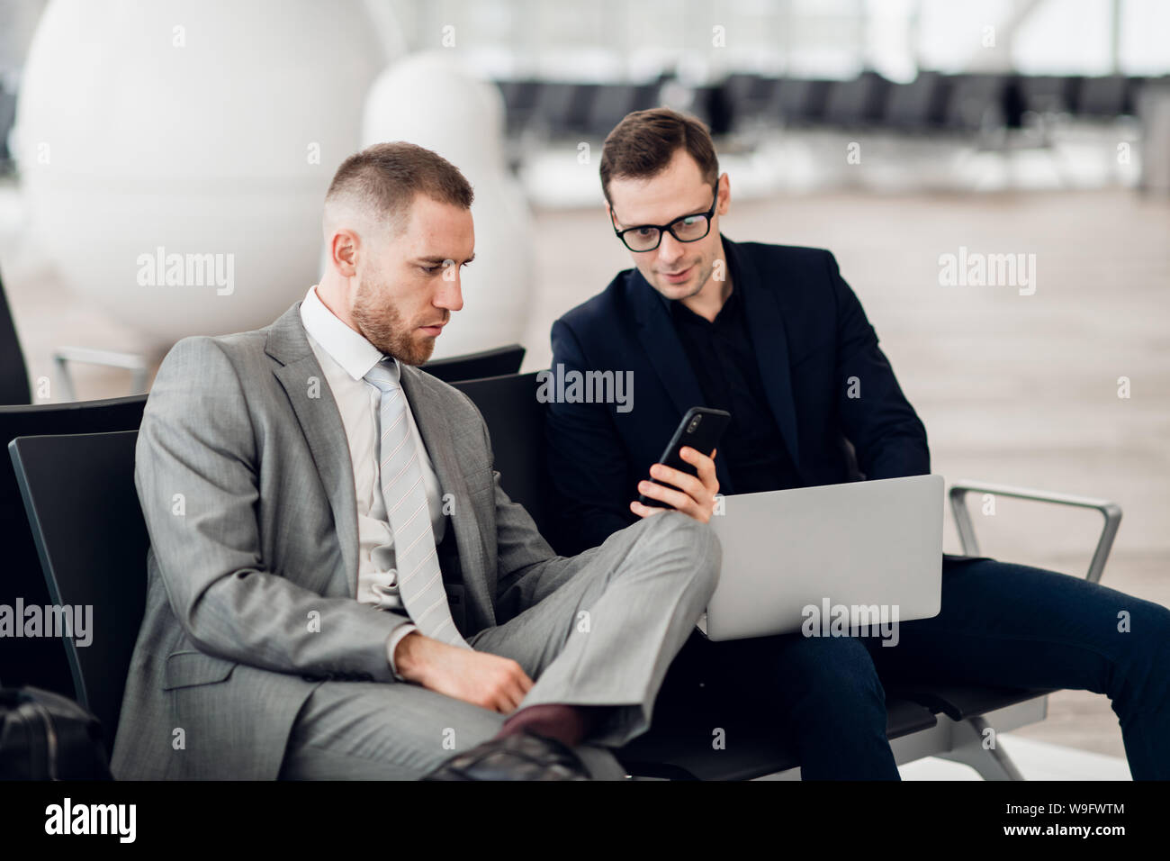 Young businessman showing a text message on his mobile phone to a male colleague at airport Stock Photo