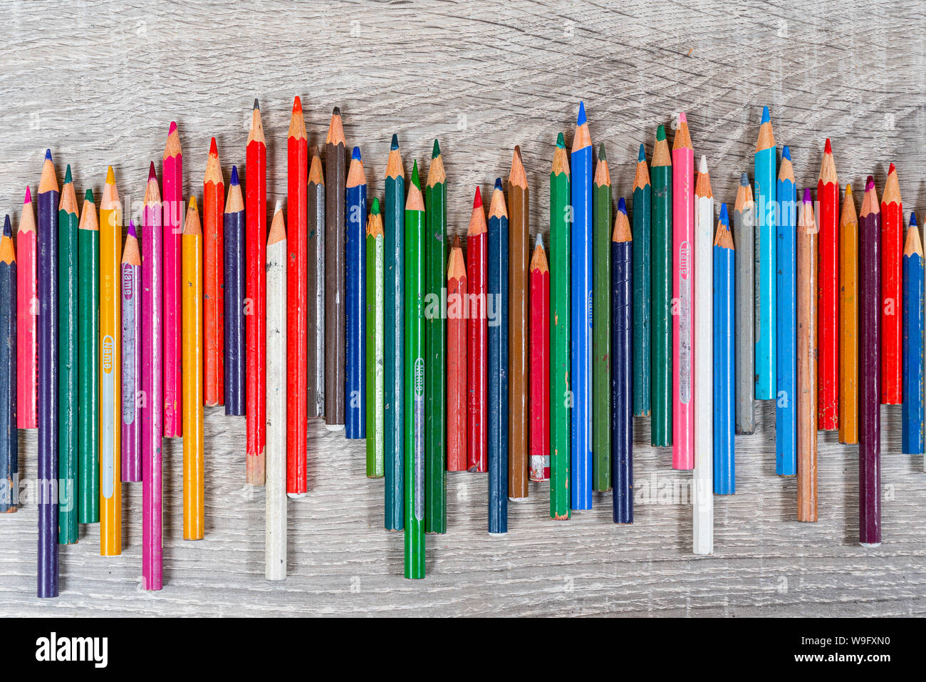 some old colored pencils lined up on a wooden table Stock Photo