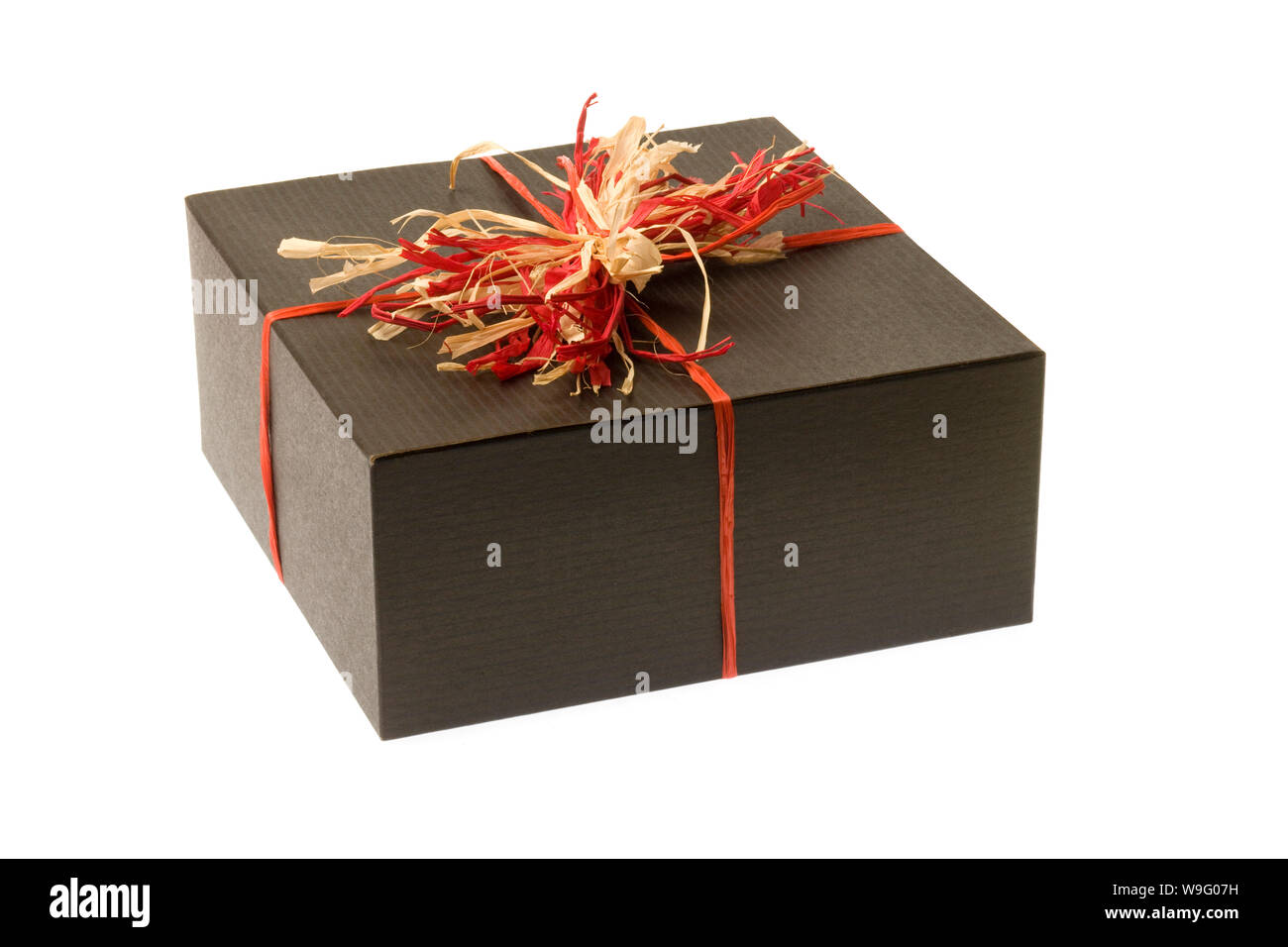 Black gift box wrapped with a red and tan natural raffia bow on a white background. Horizontal shot. Isolated on white. Stock Photo