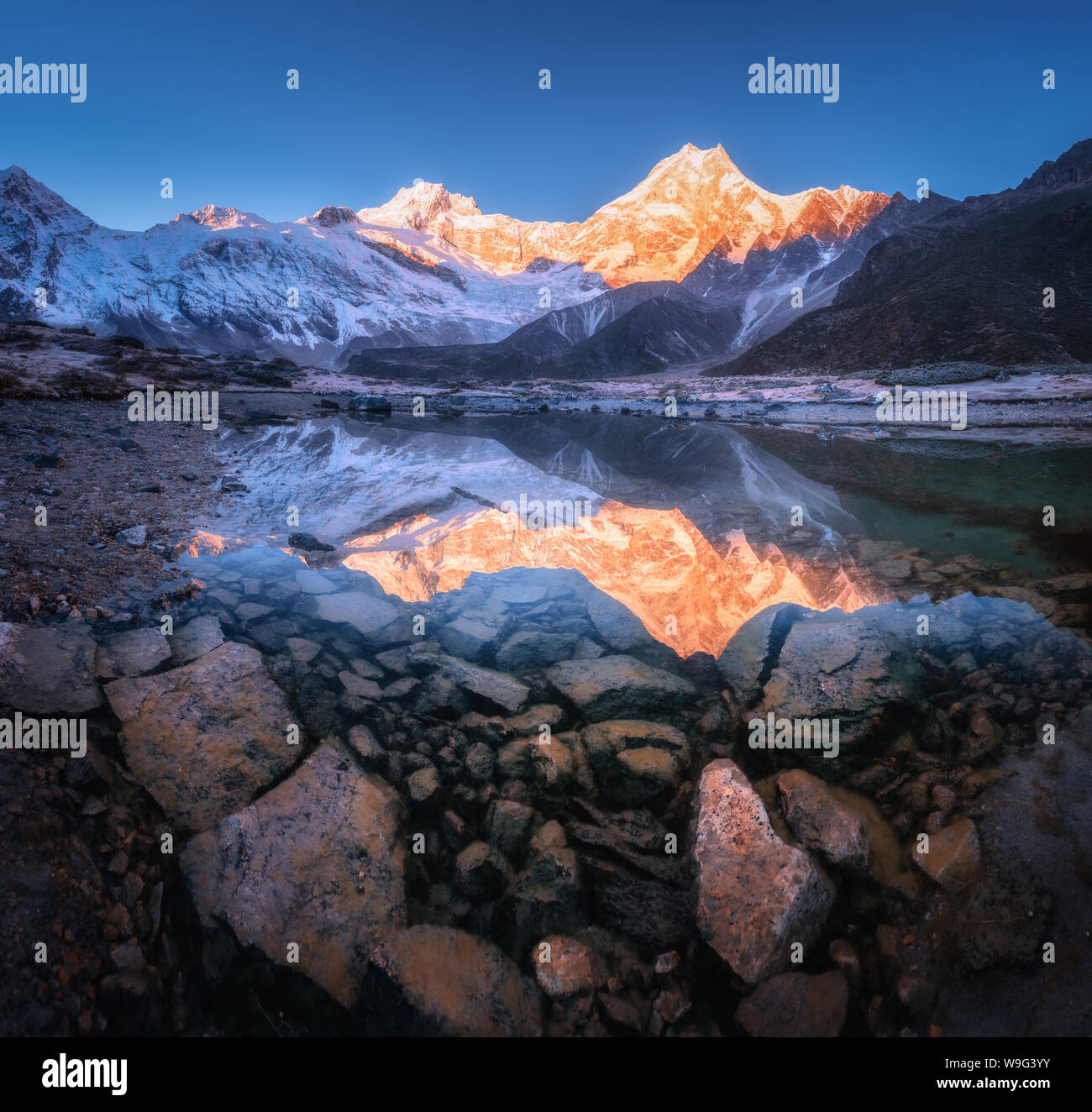 Snowy mountain with illuminated peaks is reflected in lake Stock Photo
