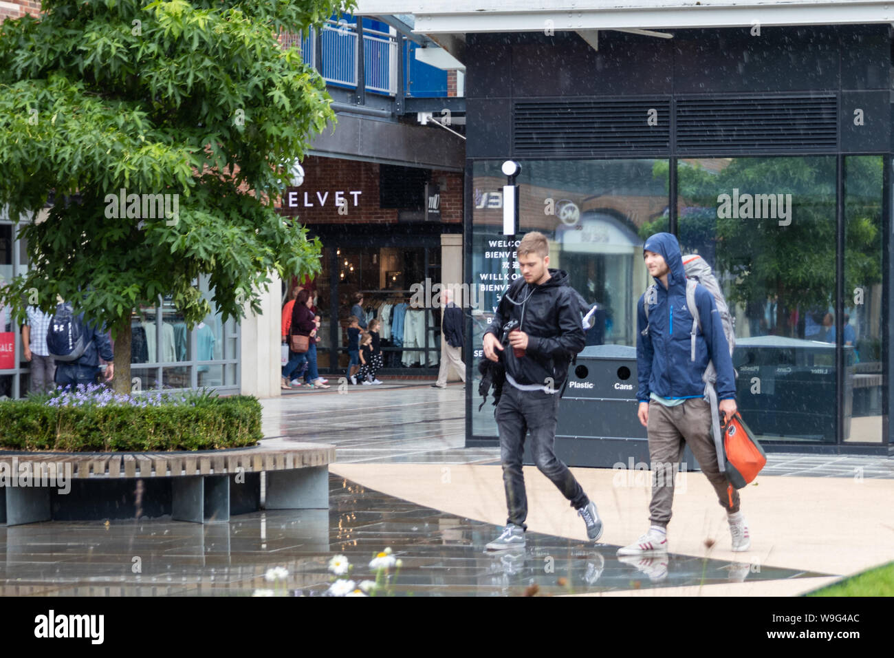 Two men walk through the rain at a shopping centre whilst shopping Stock Photo