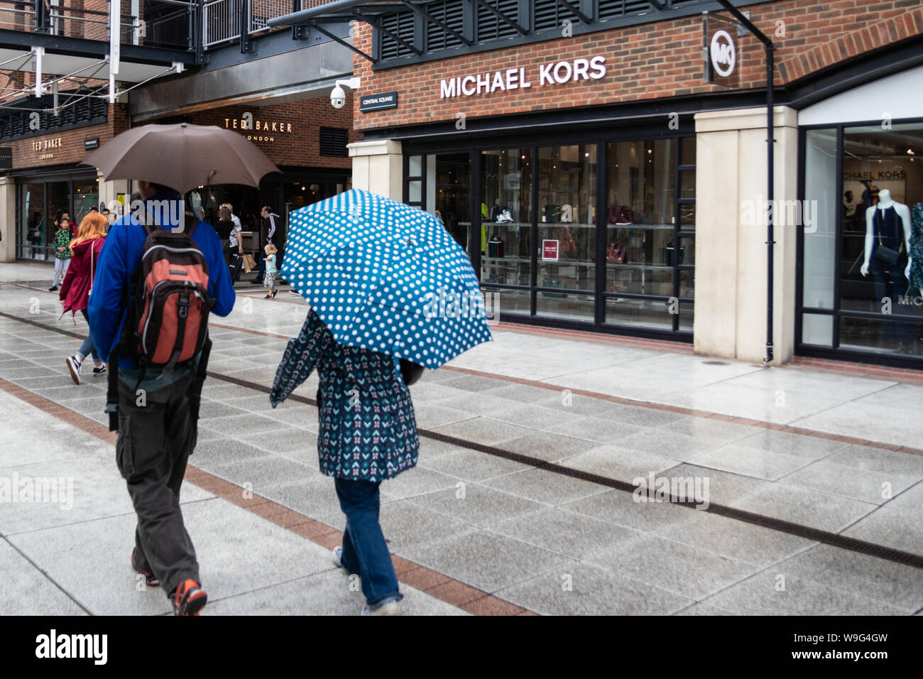 A couple take shelter from the rain under umbrellas whilst shopping Stock Photo