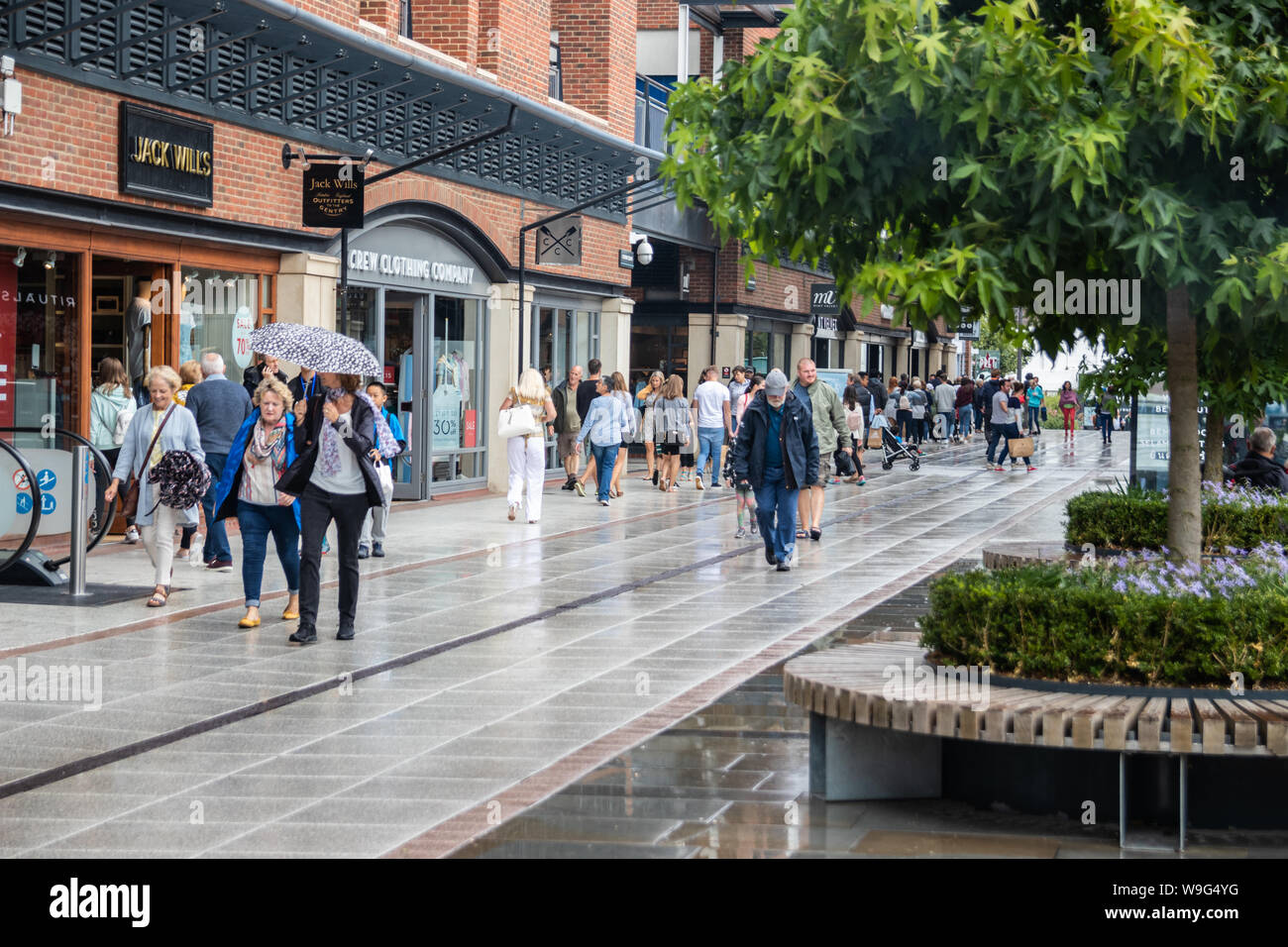 Shoppers walking through the rain at a shopping centre passing shop windows Stock Photo