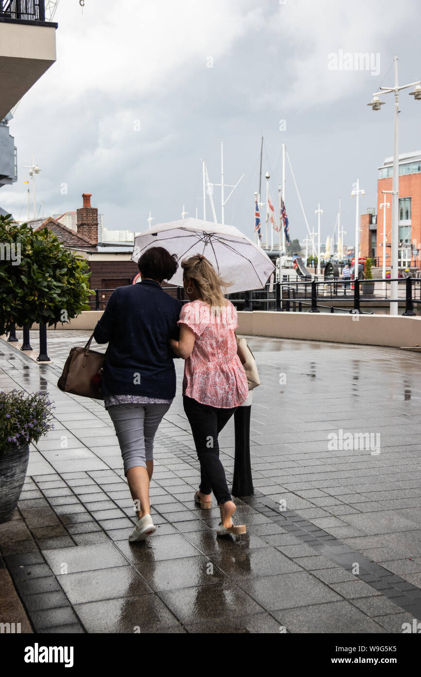 Two women taking shelter from the rain under one umbrella Stock Photo