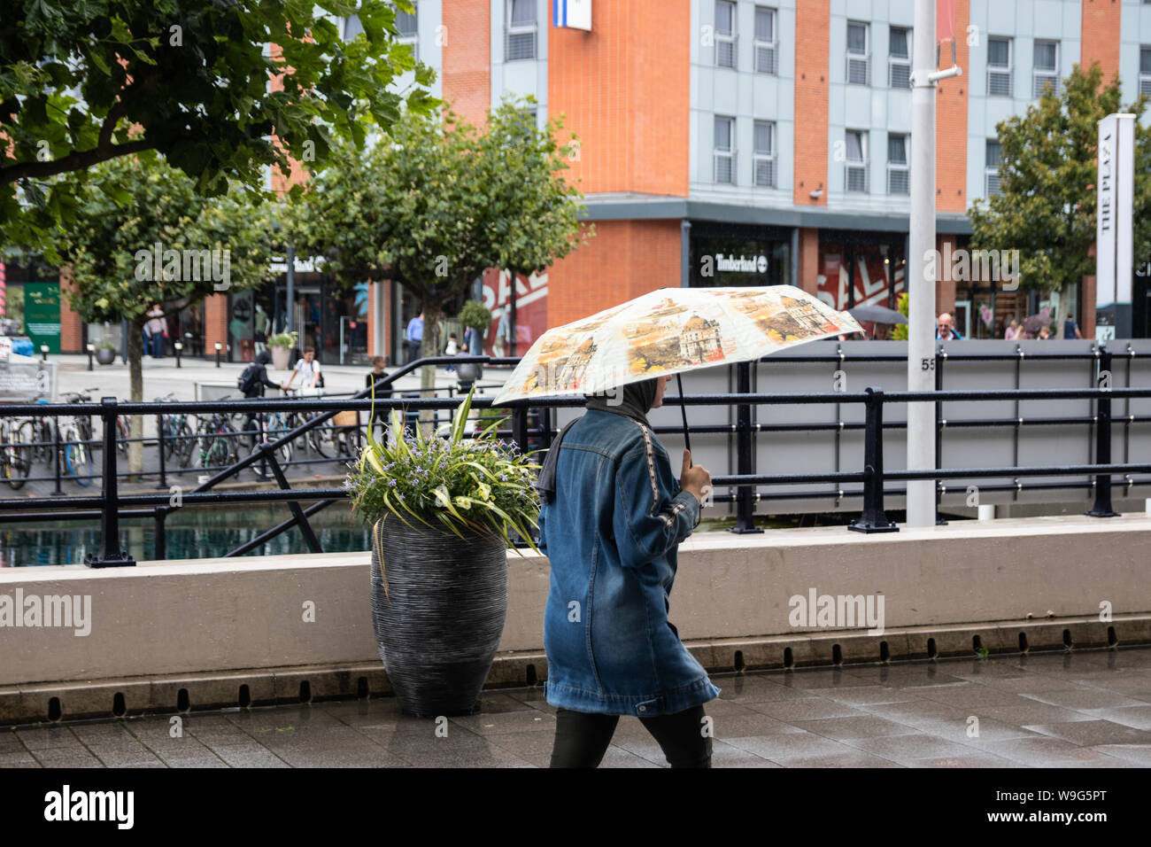 A Muslim lady wearing a hijab holding an umbrella sheltering from the rain Stock Photo