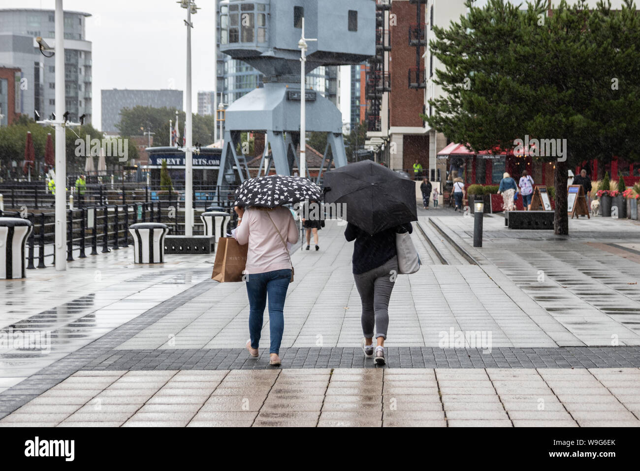 Two women taking shelter from the rain under umbrellas Stock Photo