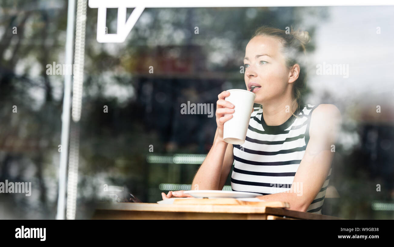Young caucasian woman sitting alone in coffee shop thoughtfully leaning on her hand, looking trough the window Stock Photo