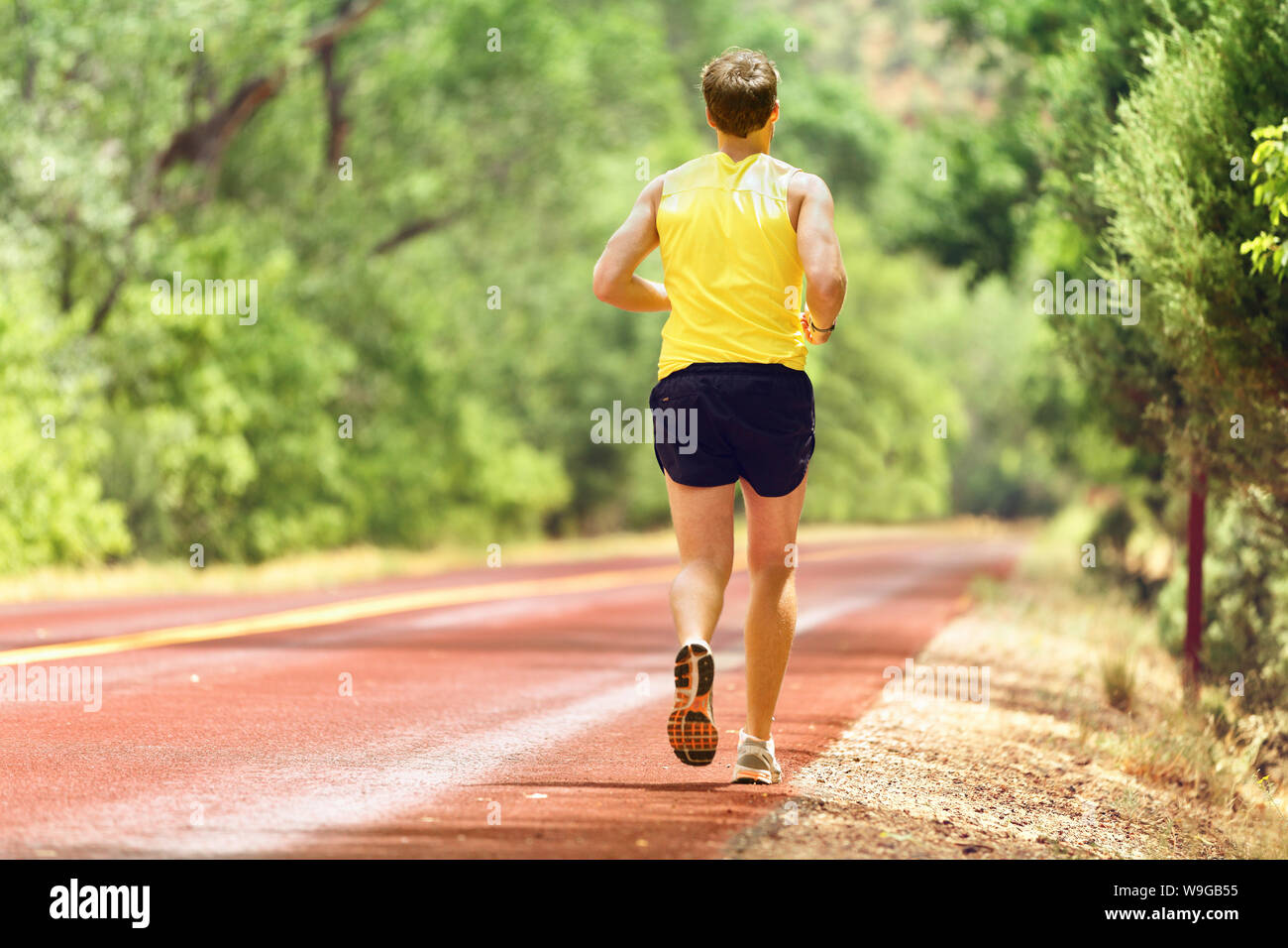 Running man runner working out for fitness. Male athlete on jogging run wearing sports running shoes and shorts working out for marathon. Full body length view showing back running away. Stock Photo