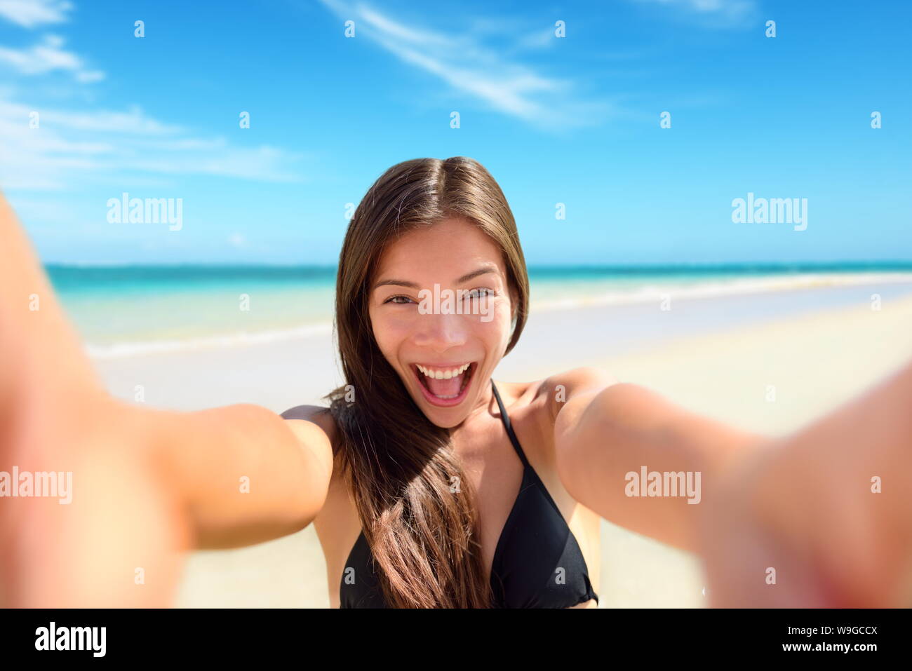 Selfie fun woman taking photo at beach vacation. Summer holiday girl happy at smartphone camera taking self-portrait on her travel vacations on pristine paradise beach. Stock Photo