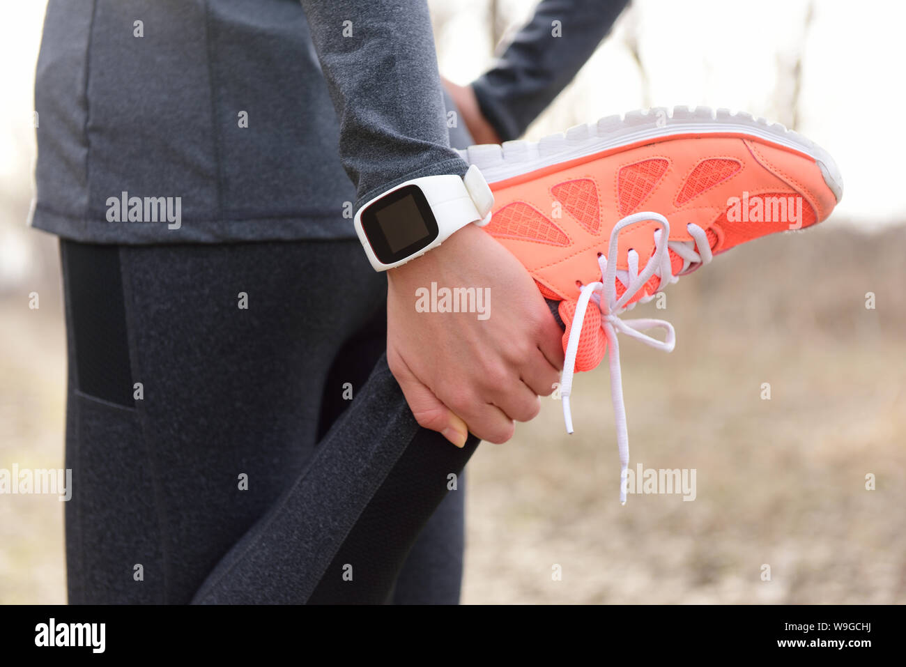 Running stretching - runner wearing smartwatch. Closeup of running shoes, woman stretching leg as warm-up before run with sport activity tracker watch at wrist to monitor the heart rate during cardio. Stock Photo