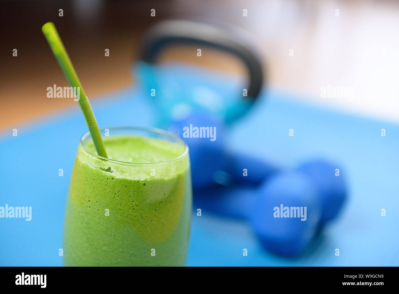 Green smoothie and dumbbells weights on yoga mat at the gym - fitness concept. Clean eating and detox with vegetable and spinach drink as part of the latest food trend in living healthy. Stock Photo