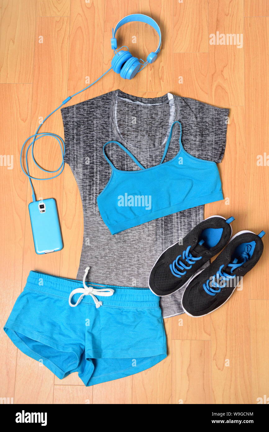 Gym outfit - workout clothing, running shoes, headphones and smartphone to listen to music while working out at the fitness center. Matching clothes, sports bra, shorts in blue and black. Stock Photo
