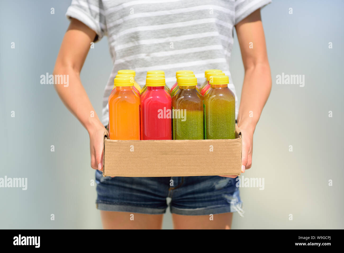 Woman holding delivery box of freshly cold pressed fruit and vegetable juice bottles. Closeup of female person carrying organic raw juices. Juicing is a food trend for diet cleanse detox. Stock Photo