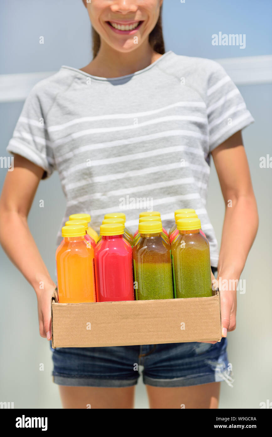 Juice detox - cleanse diet with juicing raw and organic fruits and veggies. Fresh juices delivery woman with vegetable drinks. Young girl carrying a box of juice bottles. Stock Photo