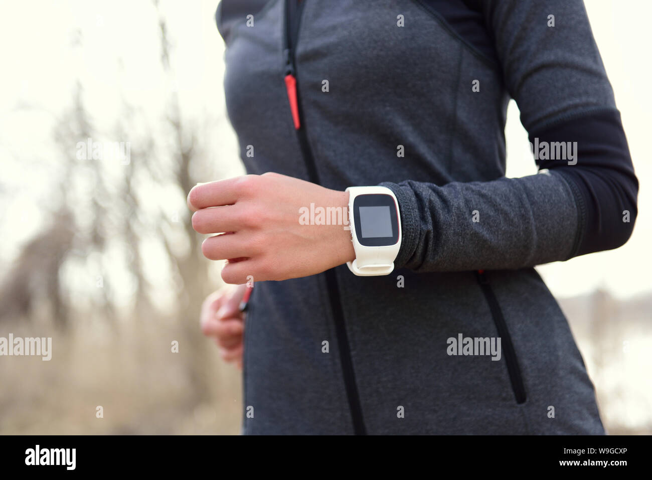 Smartwatch woman running with heart rate monitor. Closeup of female wrist wearing smart sport watch as activity tracker outdoors during cardio workout. Stock Photo