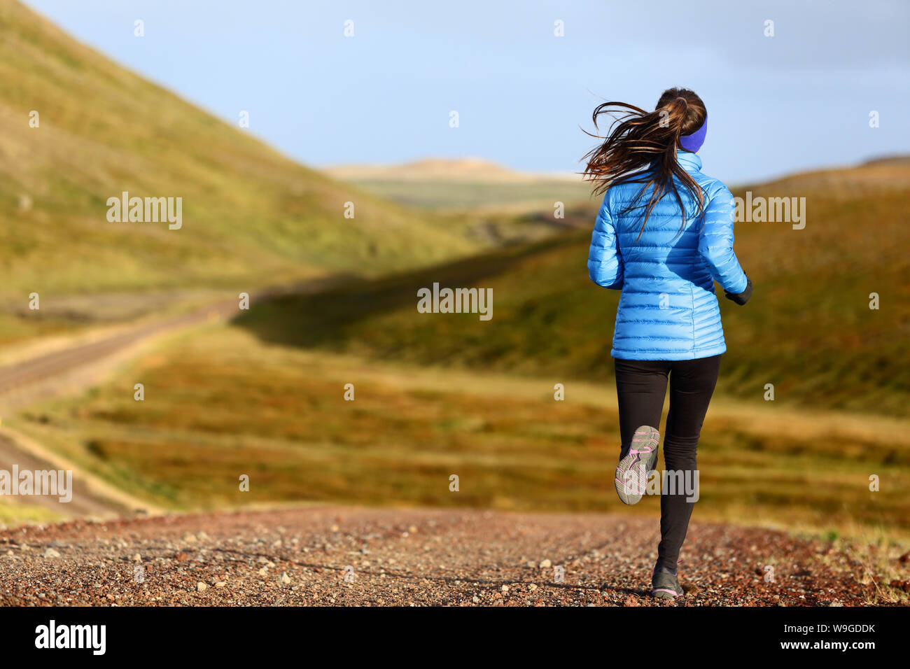 Running woman on trail run doing fitness exercise in spring autumn mountains. Person training outside in cold weather in blue sportswear. Stock Photo