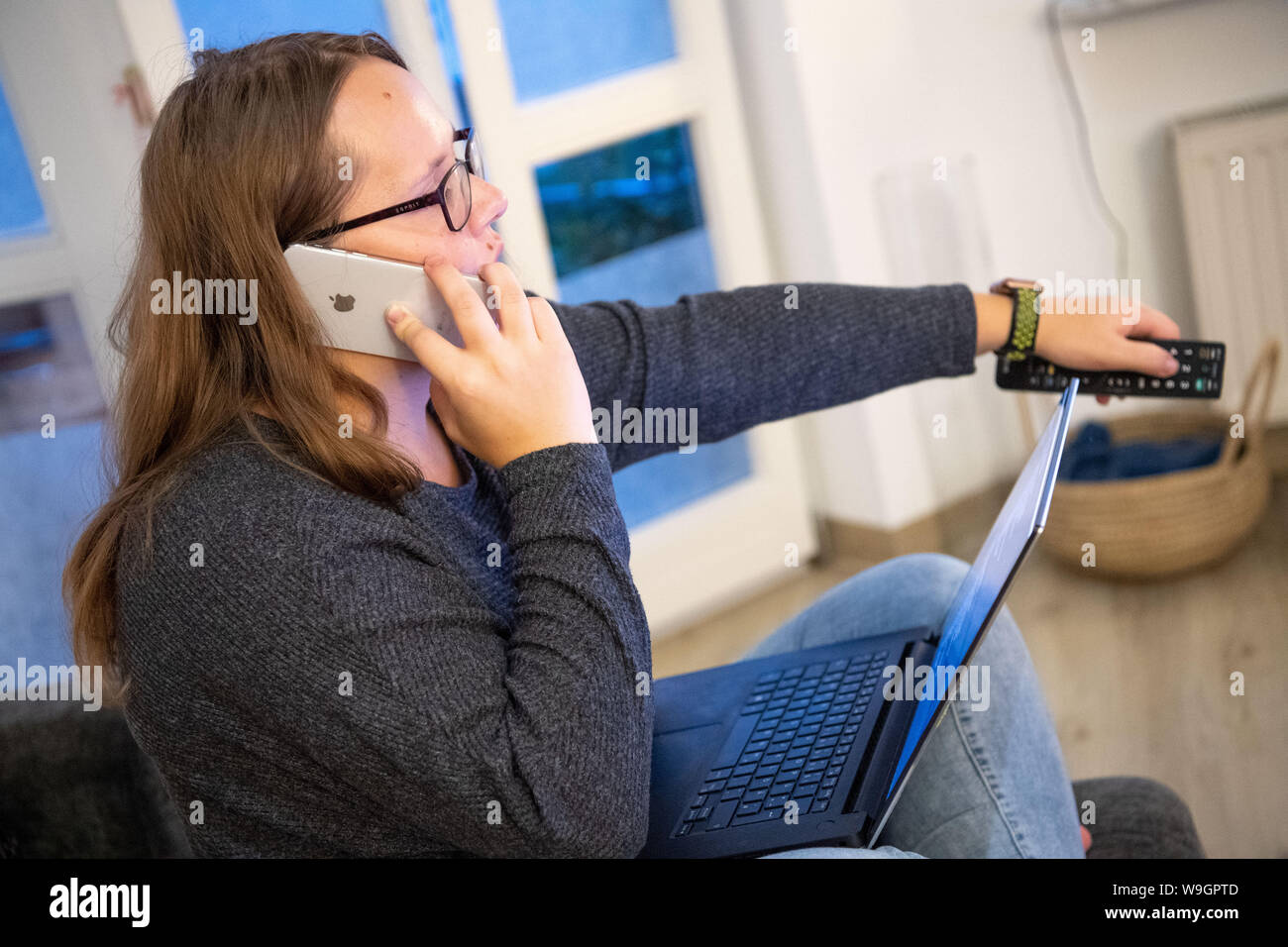 Garching, Germany. 12th Aug, 2019. A woman on the phone operates a television, in front of her is an open laptop. Women are often said to be the better multitasker. Scientifically, that's bullshit. (Zu dpa: 'In multitasking men are just as good as women') Credit: Lino Mirgeler/dpa/Alamy Live News Stock Photo