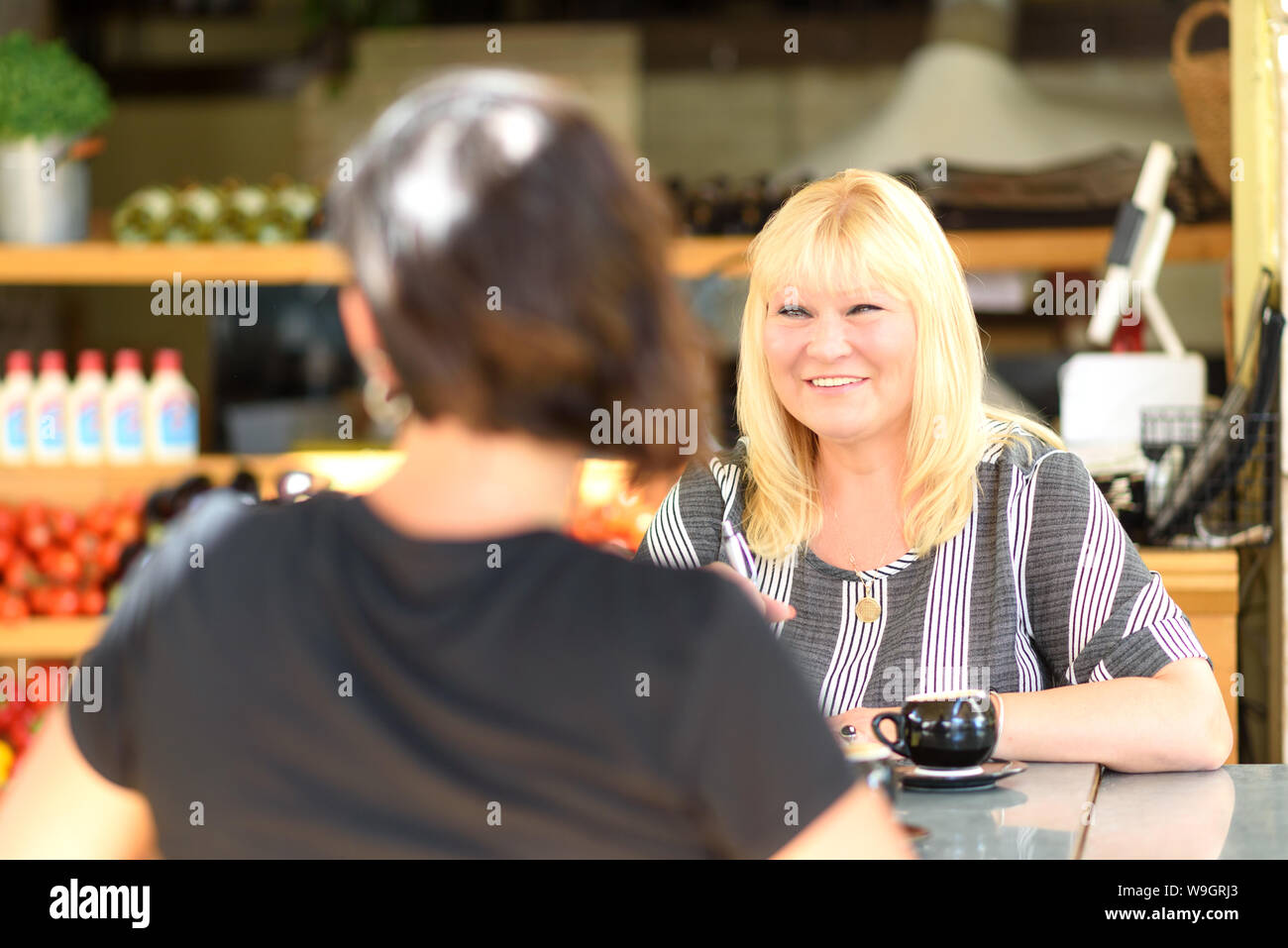 Two happy smiling girlfriends having a cup of coffee in coffee house. Psychologist with patient in cafe. Portrait of middle aged woman professional realtor or advisor consulting young happy girl. Stock Photo