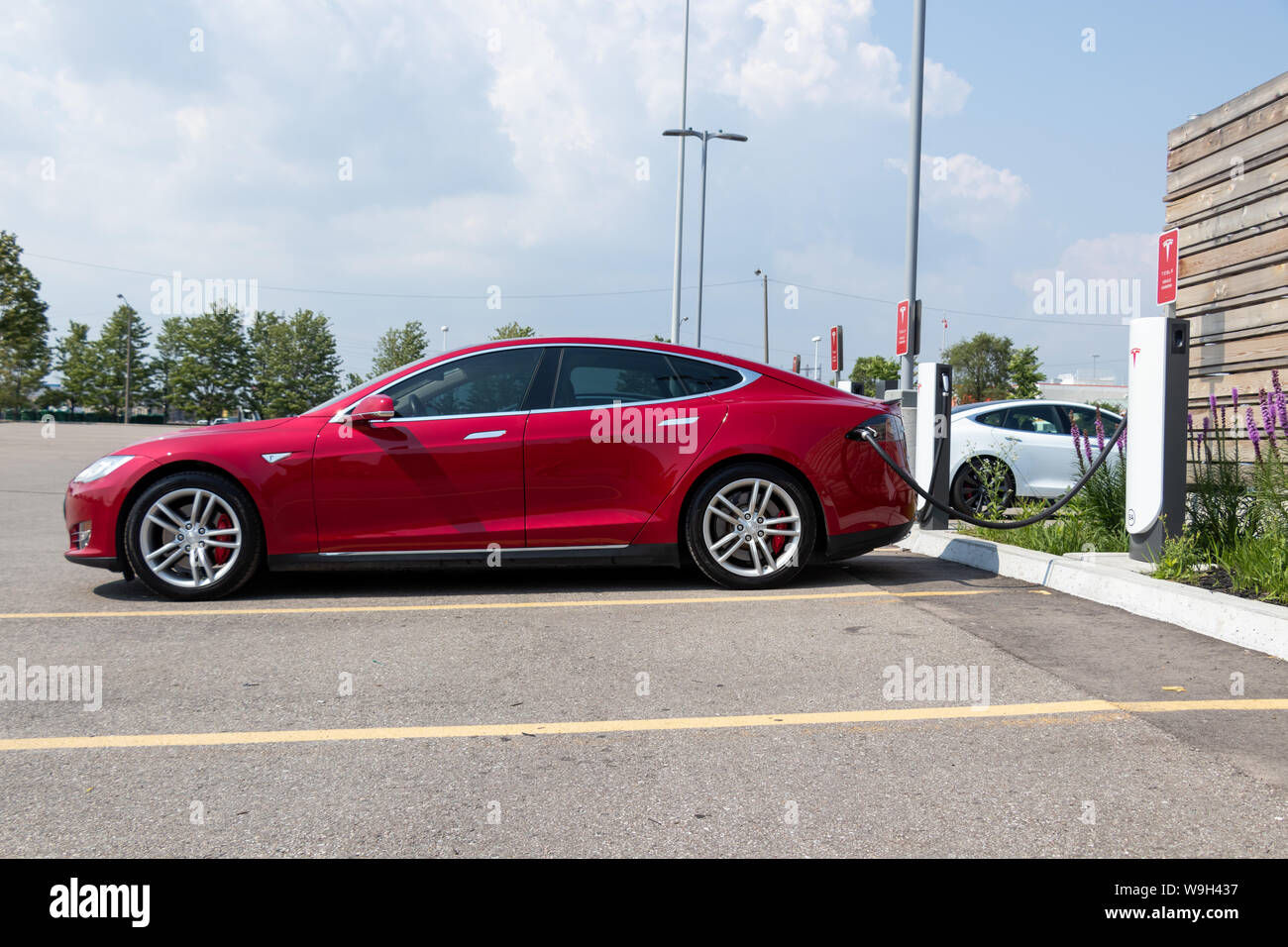 Red Tesla Model S plugged-in, charging at Tesla Urban Supercharger. Stock Photo