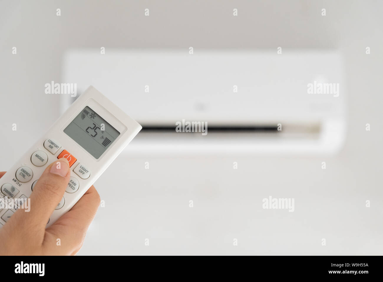 woman hand holding remote controller directed on the air conditioner inside the room and set at ambient temperature,25 degrees celsius. Stock Photo