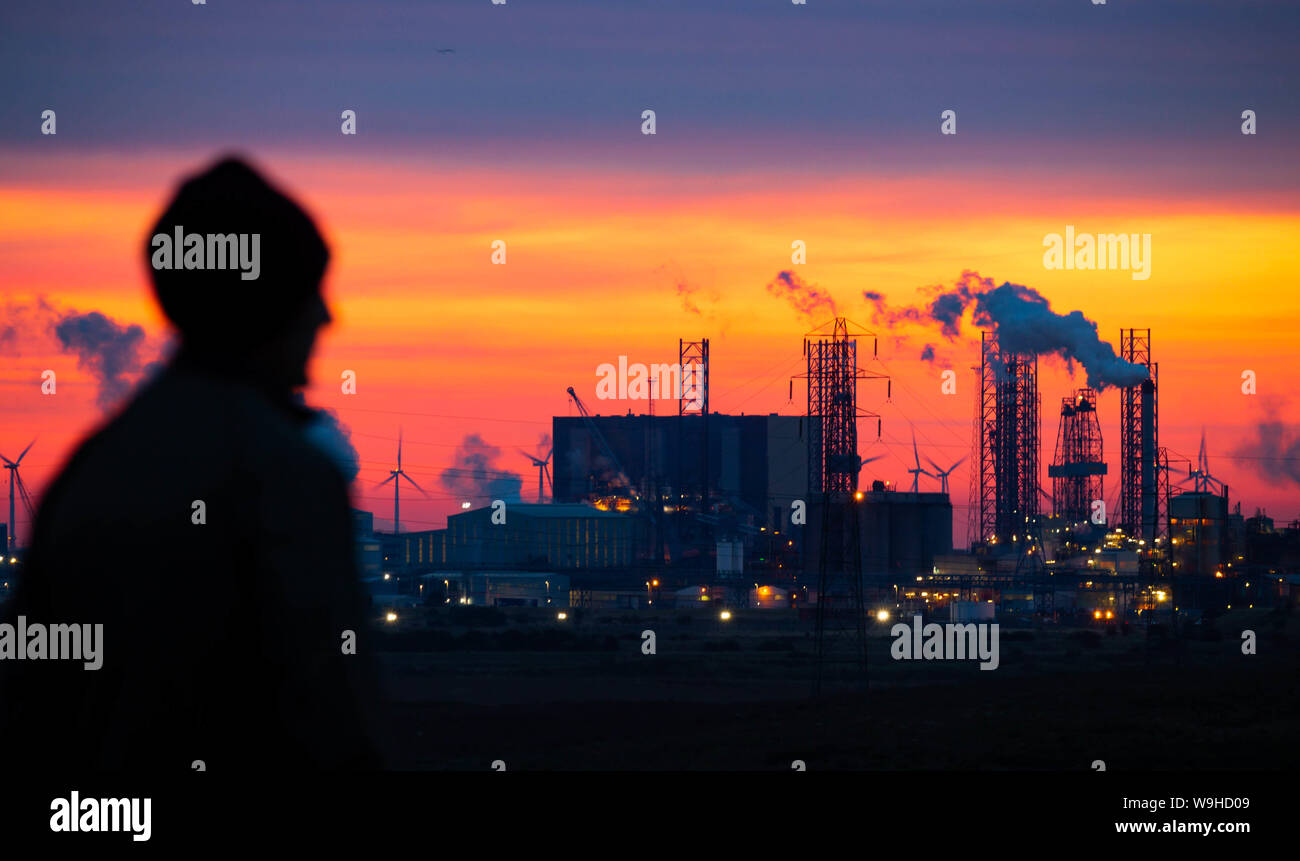 A walker looks out over Teesmouth Nature Reserve as the sun rises into thick cloud behind Hartlepool nuclear power station. UK Stock Photo