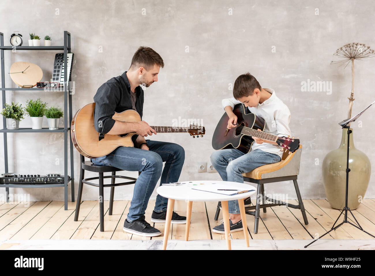 Two guys of different ages sit on chairs with guitars in their hands