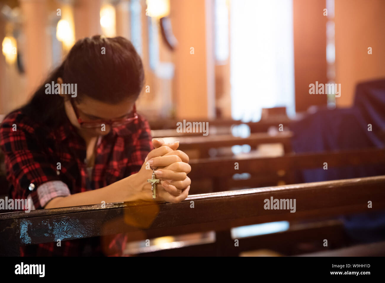Young woman sits on a bench in the church and prays to God. Hands ...