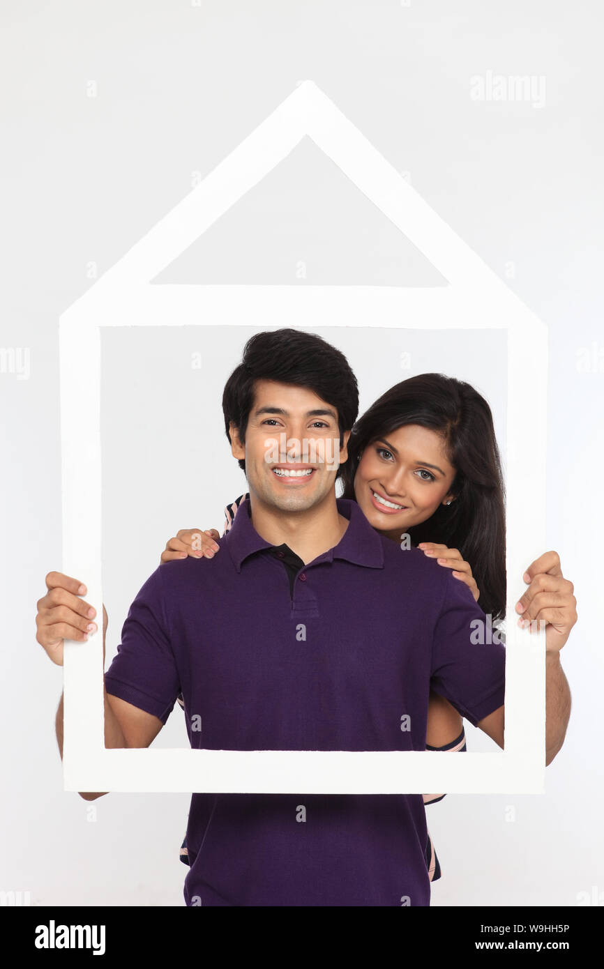 Young couple holding a dream home shape frame Stock Photo - Alamy