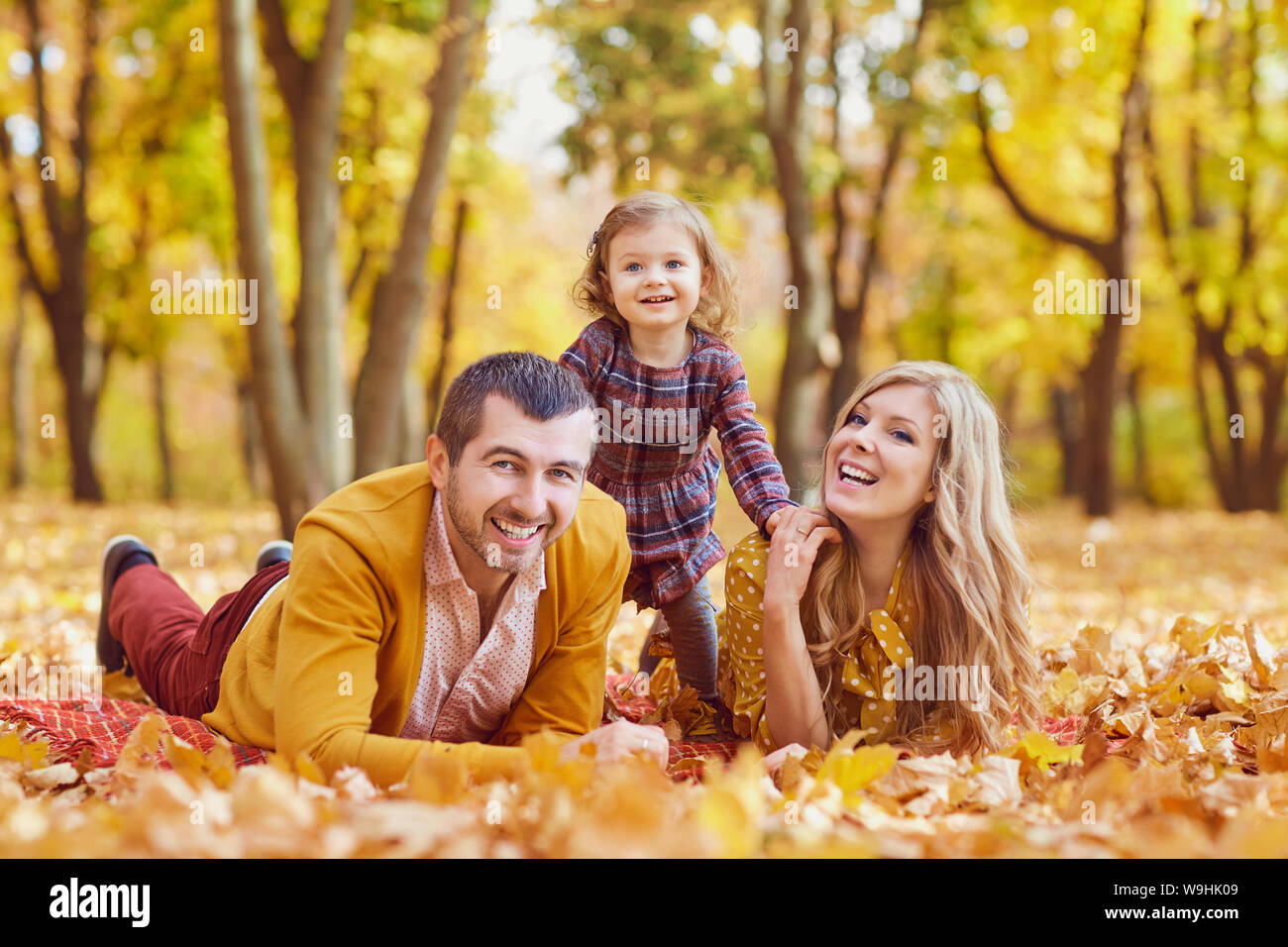 Family lying on yellow leaves in the park in autumn. Stock Photo
