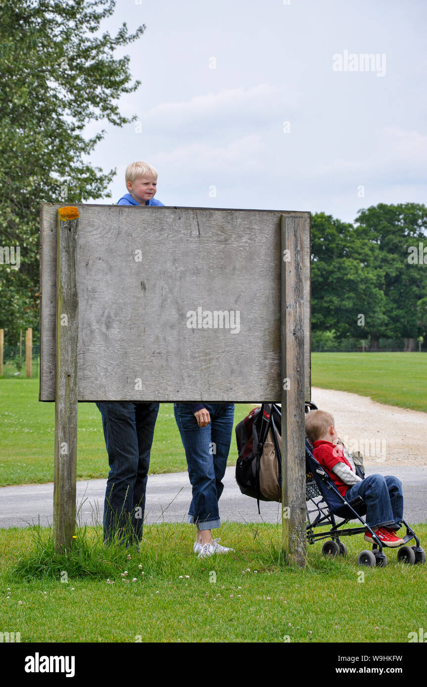Optical illusion. Apparently huge child behind a sign. Adult legs with little boy's head. Visual illusion obscured behind board. Family in park Stock Photo